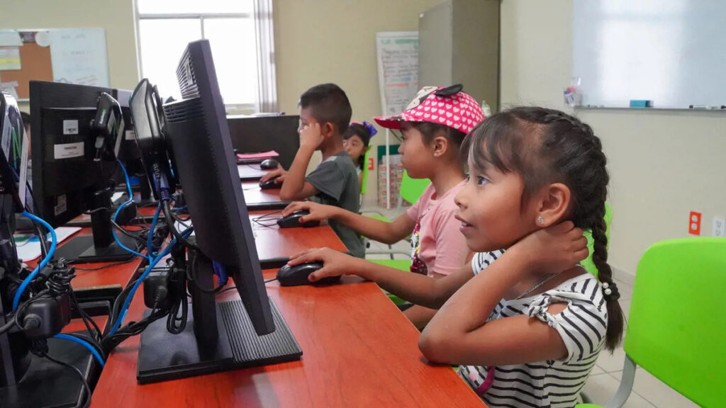 Children International's digital transformation is evident as a diverse group of children, seated at desks, actively engage with educational software and digital tools on computer screens, fostering learning and exploration.